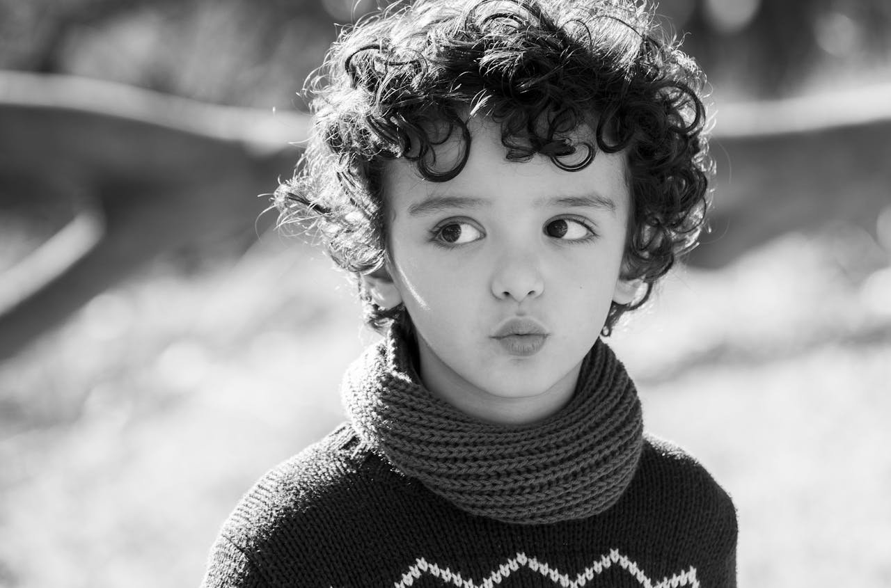 hero-gallery-03 Monochrome image of a child with curly hair wearing a scarf and sweater outdoors.